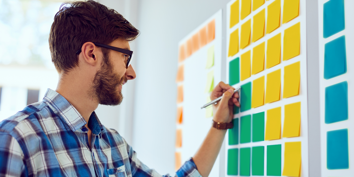 man writing on a brainstorm board with sticky notes