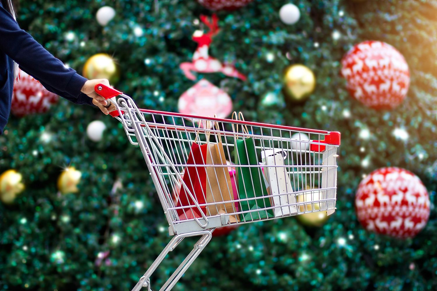 Christmas shopping - woman shopper with bags in shopping cart on holidays ornament and christmas tree on street background