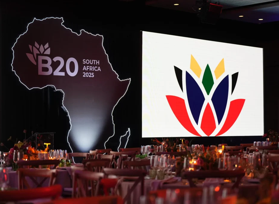 Stage with B20 South Africa 2025 logo, Africa outline, C2FO Early Payments emblem beside set tables.