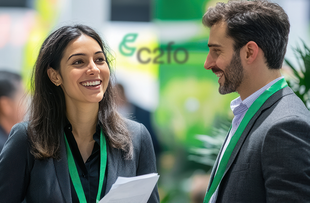 Two professionals with green lanyards smile and talk at a business event with a