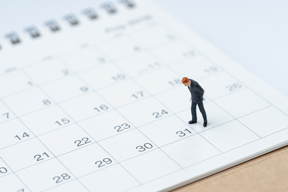 A small figurine of a man in a suit stands on a 2026 calendar, appearing to consider the true cost of each date.