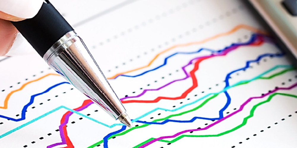 A pen points at a paper with colorful, wavy line graphs illustrating financial literacy trends.